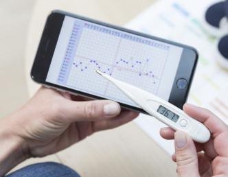 woman checking bbt thermometer and consulting charting app for ovulation and pregnancy (PCOS)